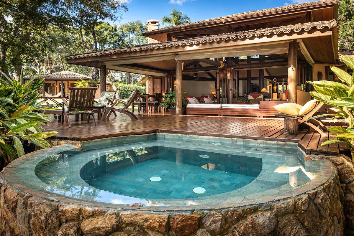 Deck de madeira com piscina de pedra, casa aberta e vista para o jardim