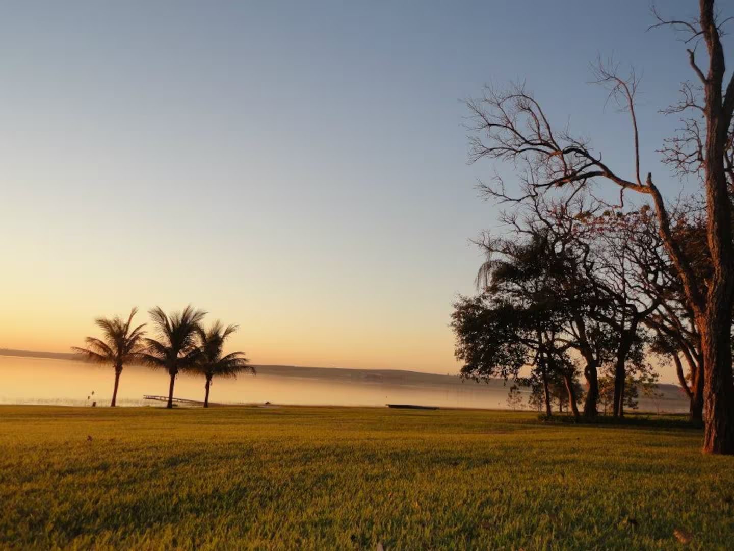 Gramado descendo até a represa ao amanhecer, pé na areia